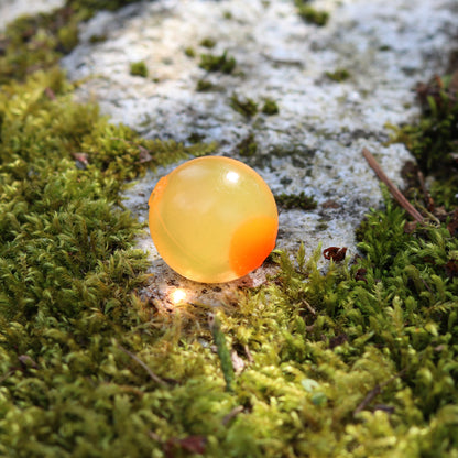 Glowing orange embryo soft bead with UV-enhanced orange dot detail, shown on a mossy forest floor background. double natural soft beads